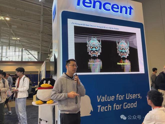 图片展示了腾讯在活动现场展示混元3D 2.1模型的场景，屏幕对比呈现混元3D 2.0与2.1版本的3D模型效果，背景有腾讯品牌标识与标语，人物正在进行讲解。