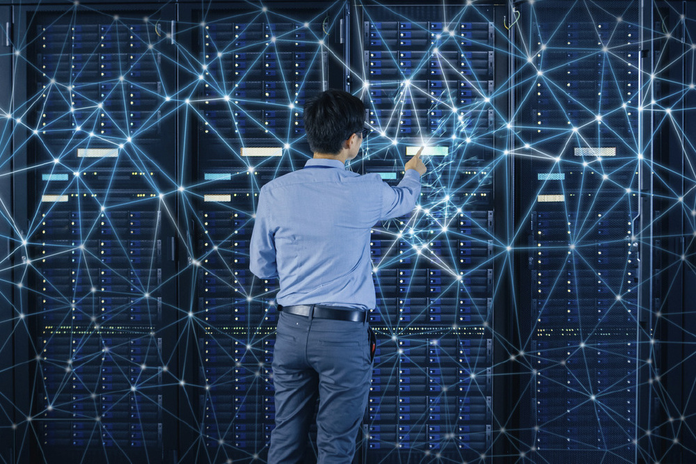 一名技术人员背对镜头操作服务器设备，背景有蓝色网络节点连线构成的科技感界面，呈现AI技术相关的数据中心场景。