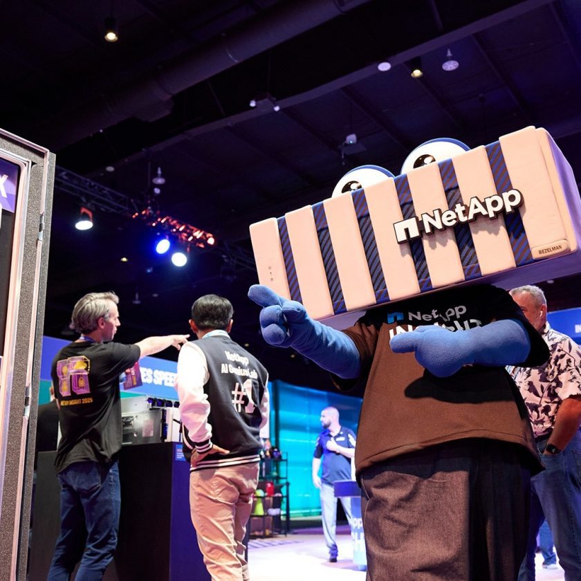 科技展会现场中，身着NetApp品牌吉祥物服装的人物与其他人员互动，背景可见舞台布置与设备展示，呈现科技企业品牌活动场景。