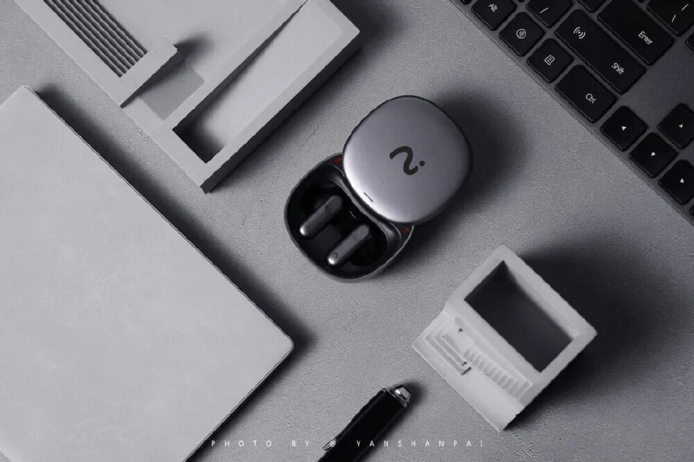 展示集成先进语音交互技术的AI耳机产品，银色充电盒内配有无线耳机，周围搭配办公场景元素，体现其在智能设备领域的应用潜力。