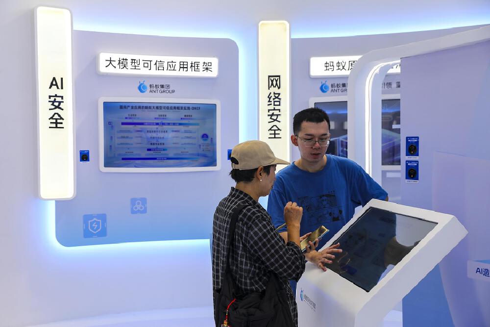 两人在展示区交流,背景有“AI安全”“大模型可信应用框架”等字样,展示蚂蚁集团相关的大模型安全应用框架技术内容。