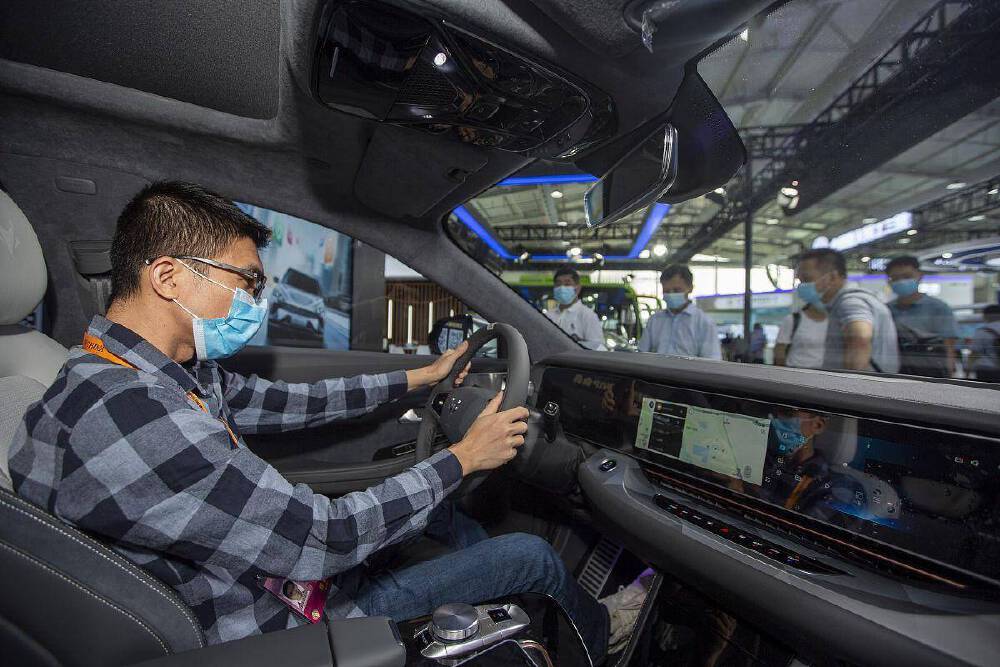 一名佩戴口罩的体验者在车内操作配备导航功能的智能座舱，中控屏幕显示导航地图，背景为展会场景，体现车载AI交互技术应用。