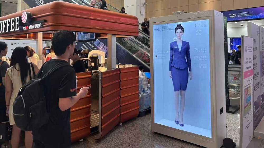 展会现场展示一位穿着蓝色职业装的AI虚拟数字人，周围有参观者互动，呈现数字人技术的实际应用场景。