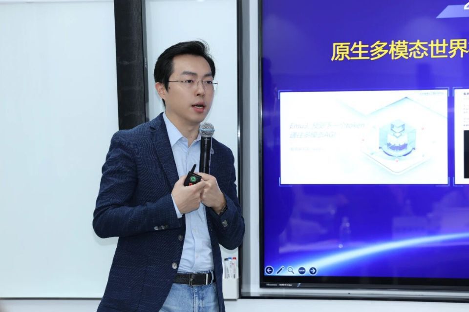 智源研究院相关人员在发布会上讲解Emu3.5多模态世界大模型，背景屏幕展示“原生多模态世界”等技术相关内容，涉及多模态AI模型研发的现场场景。